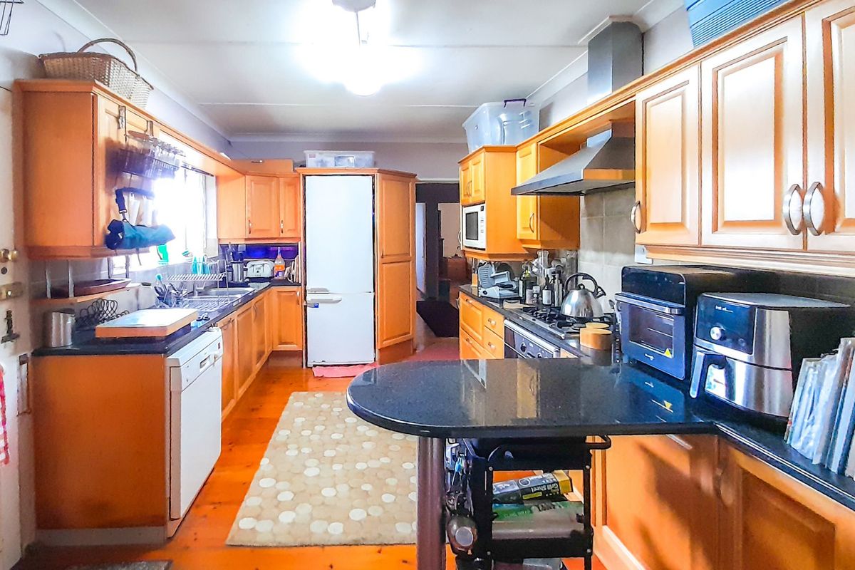 A functional kitchen featuring timber cabinetry, granite countertops, gas cooktop, and integrated stainless steel appliances with warm timber flooring.