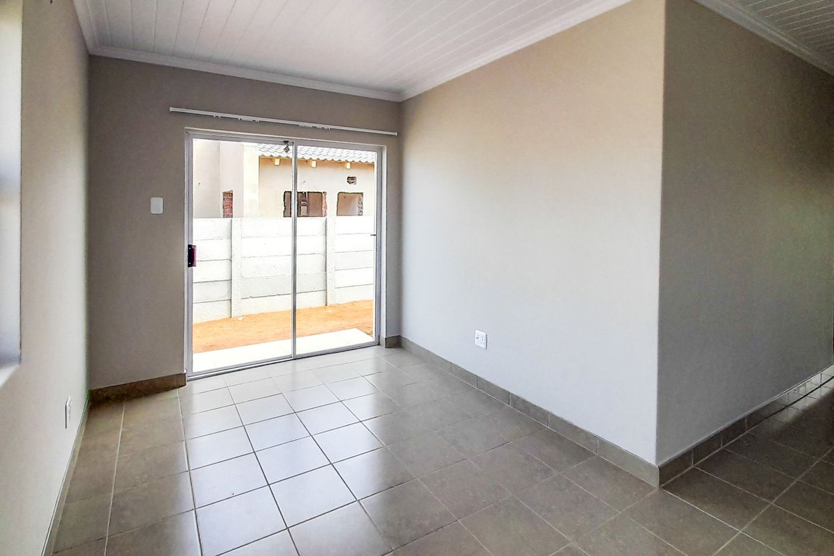 A bright, empty living area featuring neutral tiled flooring, a tongue and groove ceiling, and a sliding glass door providing access to the rear exterior.