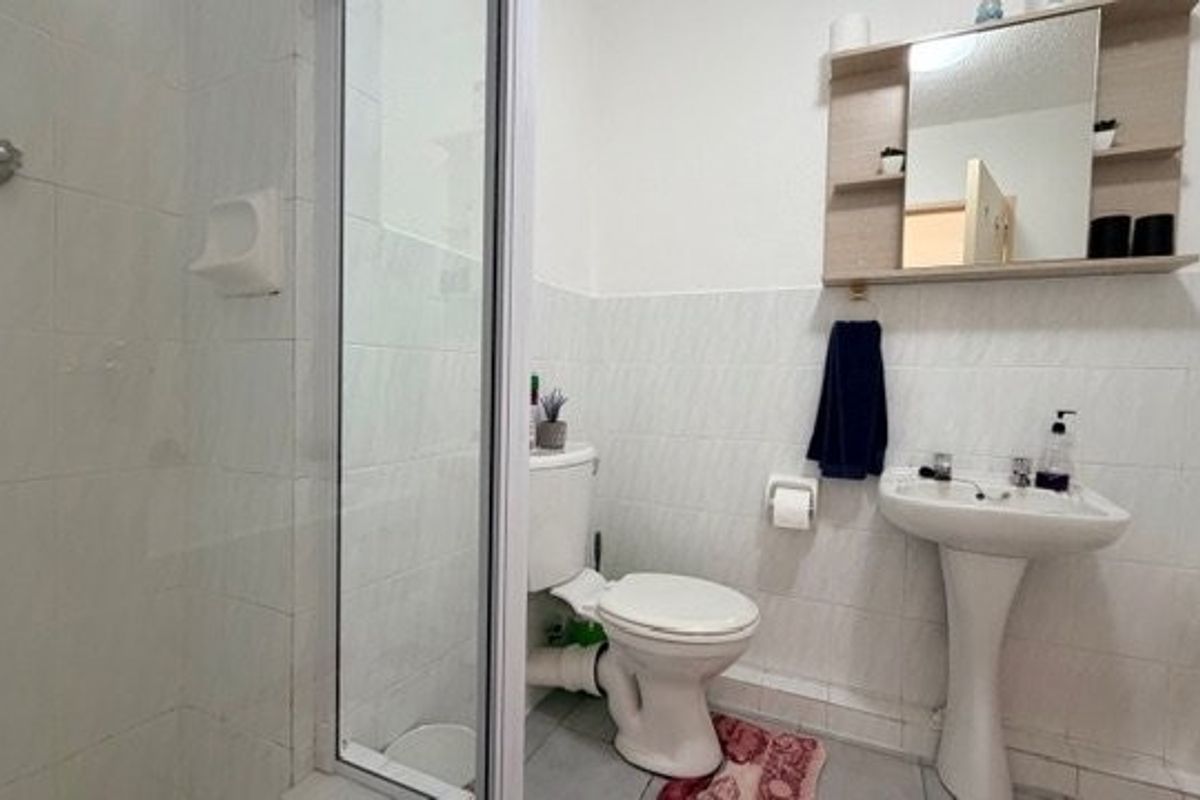 A functional bathroom featuring a pedestal sink, toilet, and a glass-enclosed shower with tiled wall finishes.
