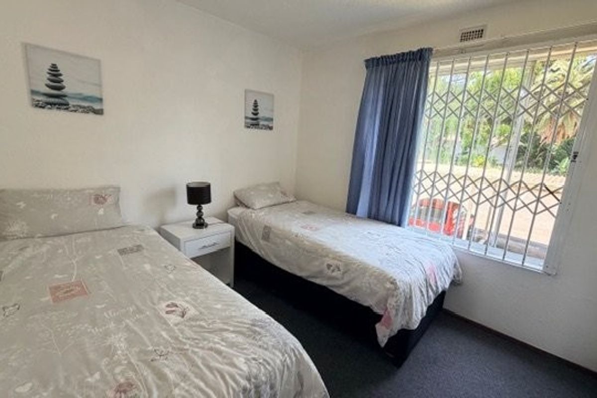 A functional bedroom featuring a window with a fitted security gate and curtain rail, providing natural light and ventilation.