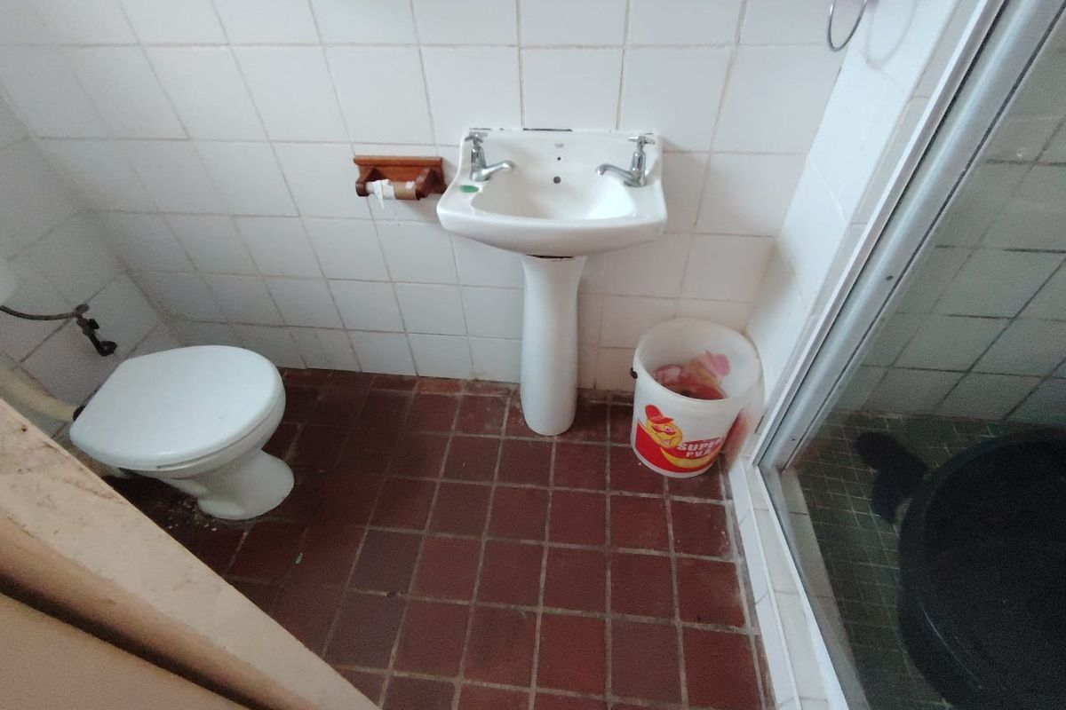 A compact bathroom featuring a pedestal basin, toilet, and shower enclosure with dated ceramic tiling throughout.
