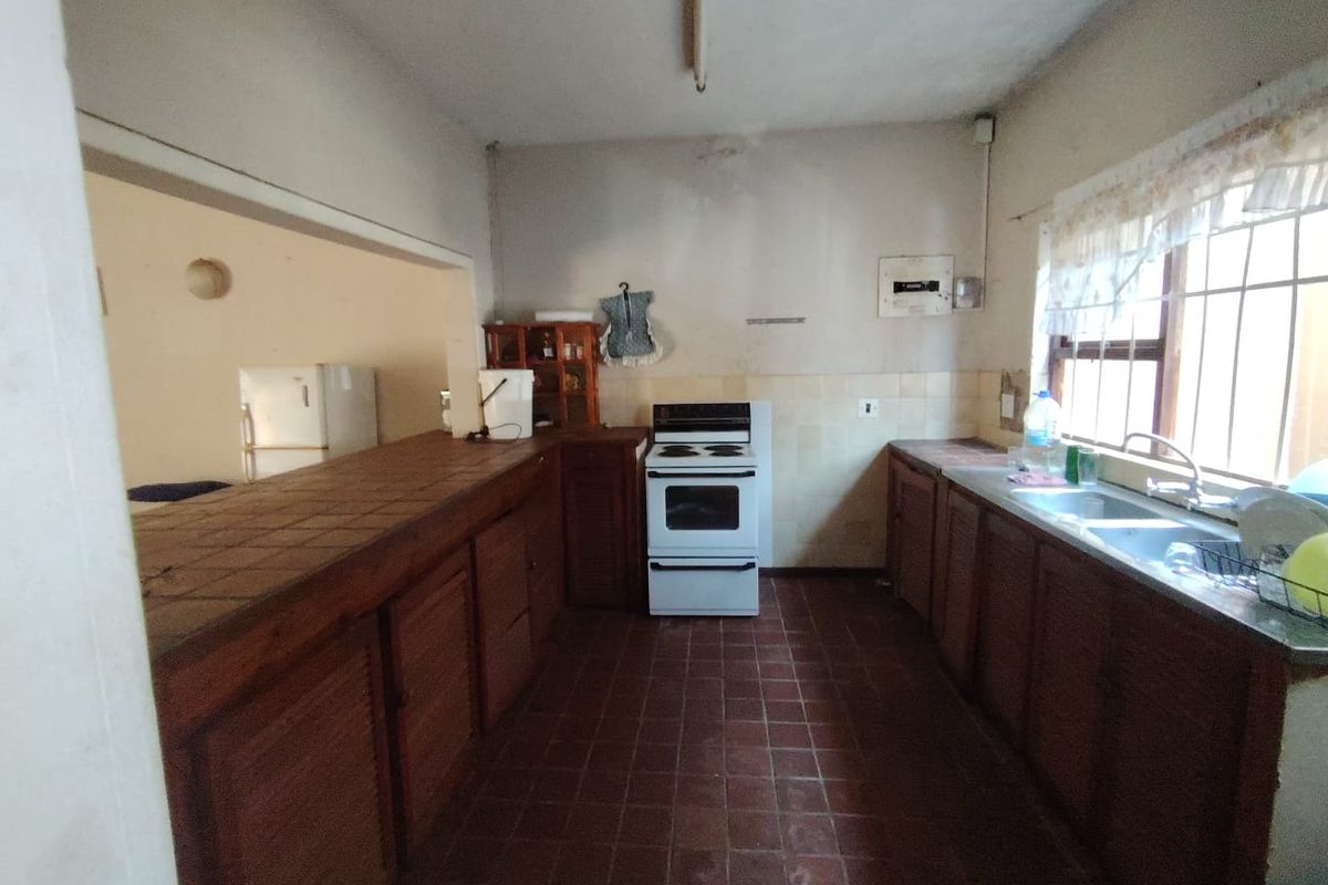 A dated kitchen featuring wooden cabinetry, tiled countertops, a double basin sink, and a freestanding stove, offering significant potential for modernization and renovation.