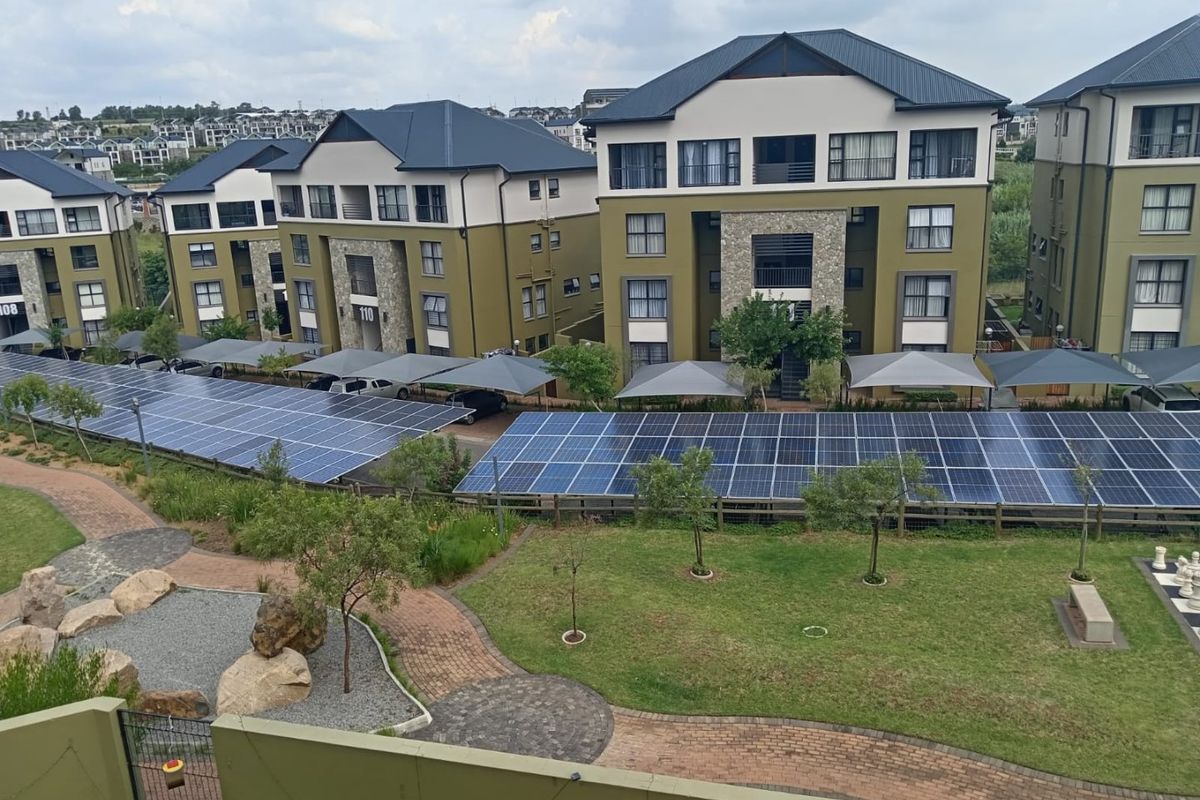 Elevated view of a well-maintained apartment complex featuring landscaped gardens, paved pathways, and extensive solar panel carports.