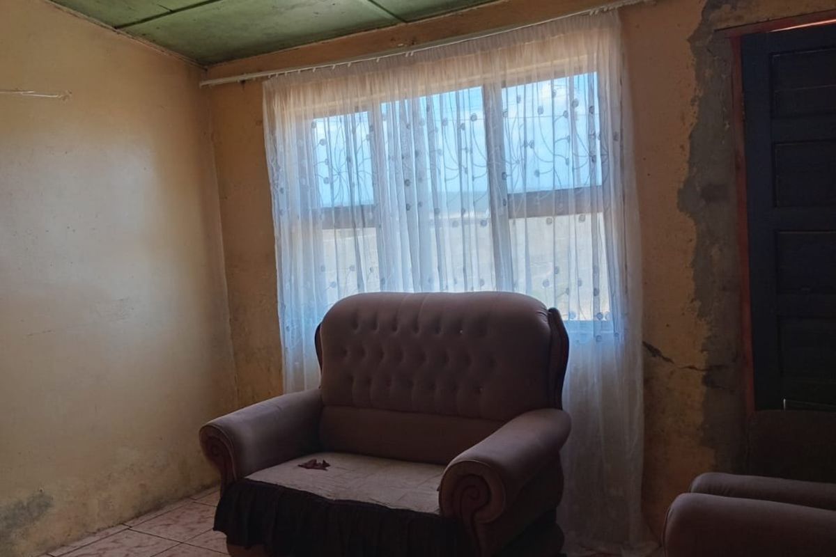 A living room featuring tiled flooring and a window, currently showing significant wear to the wall finishes and plaster.