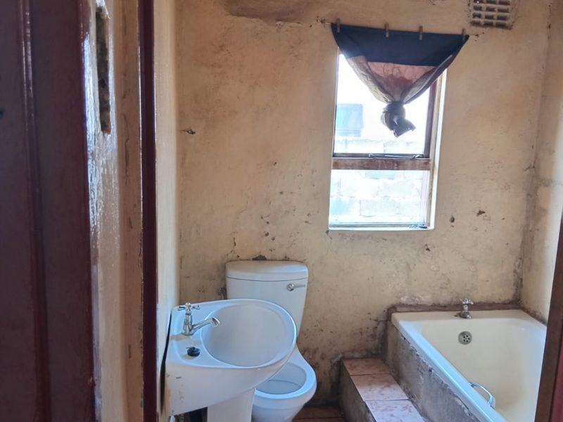 A small bathroom featuring a pedestal basin, toilet, and built-in bathtub, requiring significant renovation and wall repairs to restore functionality and aesthetic appeal.