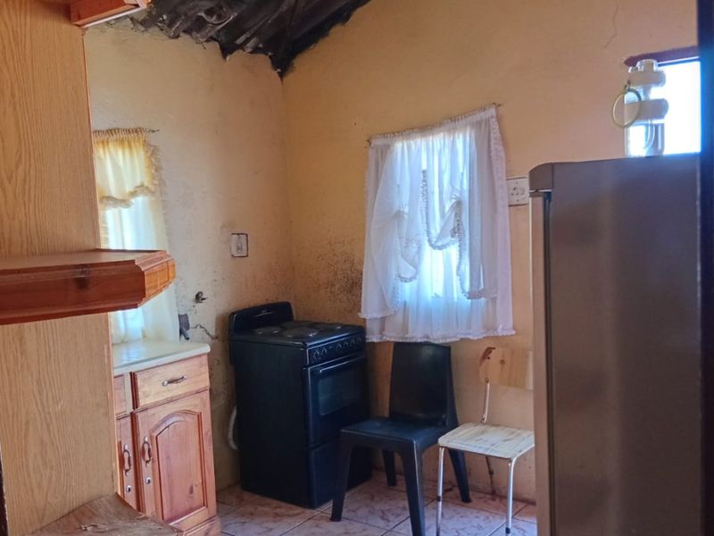 A small, dated kitchen featuring tiled floors, wooden cabinetry, and an exposed roof structure, requiring significant renovation and cosmetic updates.