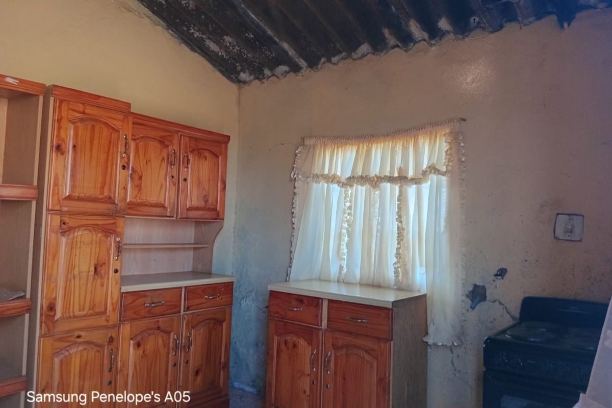 A dated kitchen area featuring wooden cabinetry and an exposed roof structure, requiring significant renovation and repair to wall finishes.