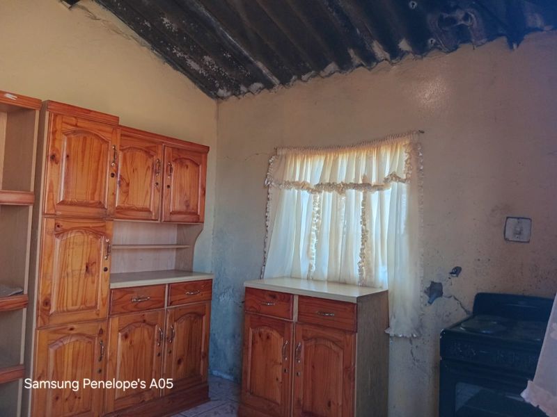 A dated kitchen area featuring wooden cabinetry and an exposed roof structure, requiring significant renovation and repair to wall finishes.
