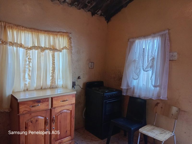 A small kitchen area featuring wooden cabinetry and a freestanding stove, requiring significant renovation and wall repairs to improve the overall condition.