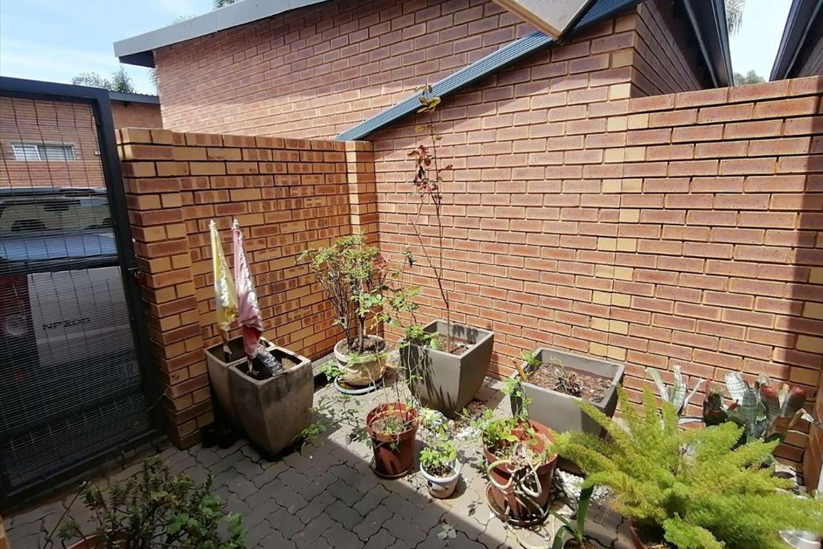 A private paved courtyard area enclosed by brick boundary walls, featuring a metal access gate and overhead shade structure.