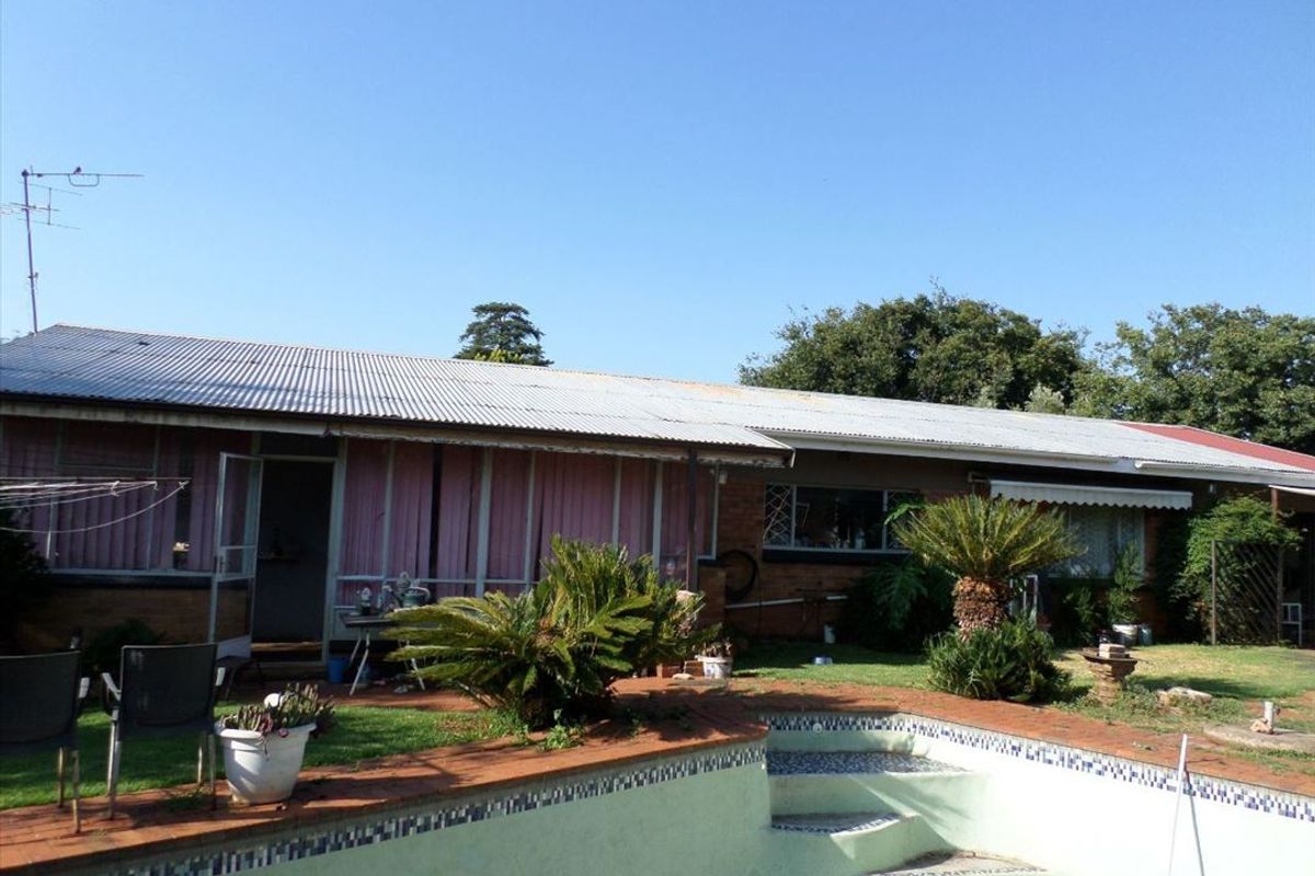 Rear view of the property featuring a swimming pool, brick exterior walls, and a corrugated metal roof.