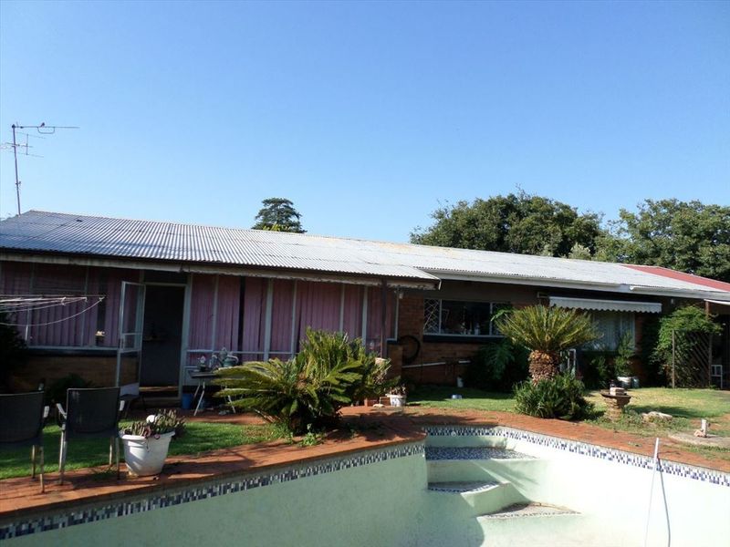 Rear view of the property featuring a swimming pool, brick exterior walls, and a corrugated metal roof.