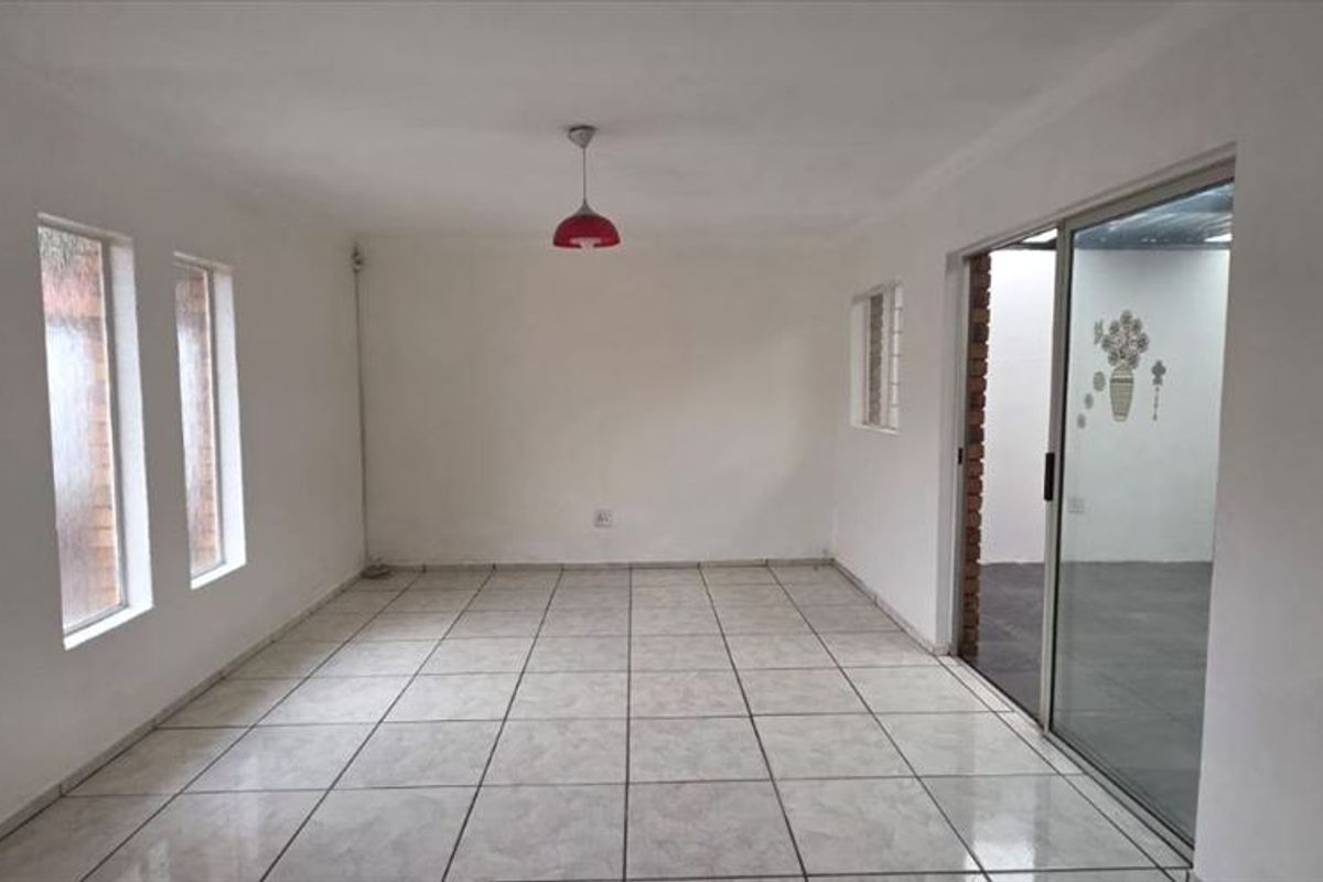An empty, neutrally painted living area featuring tiled flooring, vertical windows, and a sliding glass door leading to an adjacent space.