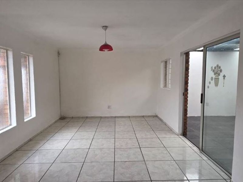 An empty, neutrally painted living area featuring tiled flooring, vertical windows, and a sliding glass door leading to an adjacent space.