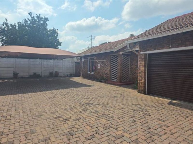 Front exterior view of the townhouse featuring a paved driveway, shade sail carport, and a single roller garage door with facebrick exterior walls.