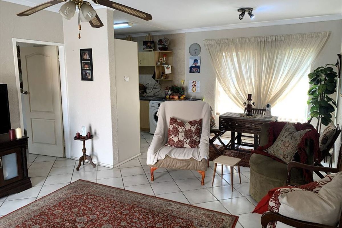 Open-plan living area featuring tiled flooring, a ceiling fan, and a partially visible kitchen space with built-in cabinetry.