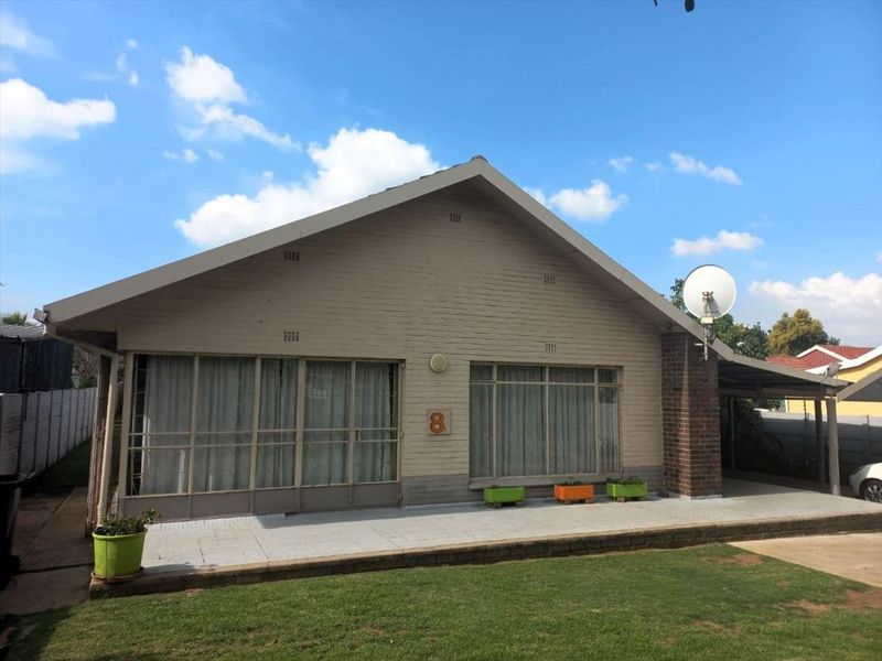 Front elevation of a single-story brick house featuring a concrete patio, large sliding glass doors, and a tiled roof.