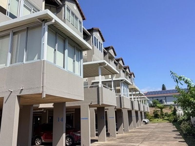 Exterior view of a multi-story apartment complex featuring covered parking bays on the ground level and enclosed balconies on the upper floors.