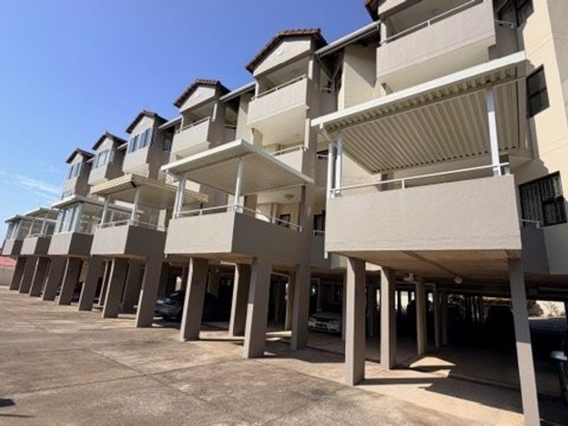 Rear elevation of a multi-story apartment complex featuring elevated balconies with covered patios and ground-level parking bays.