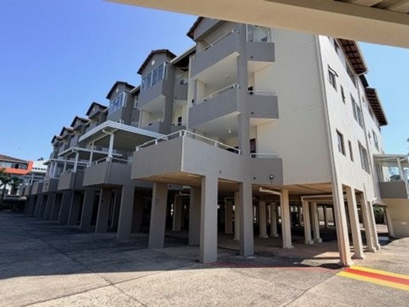 Exterior view of a multi-story apartment complex featuring stilted construction, private balconies, and a paved driveway area.