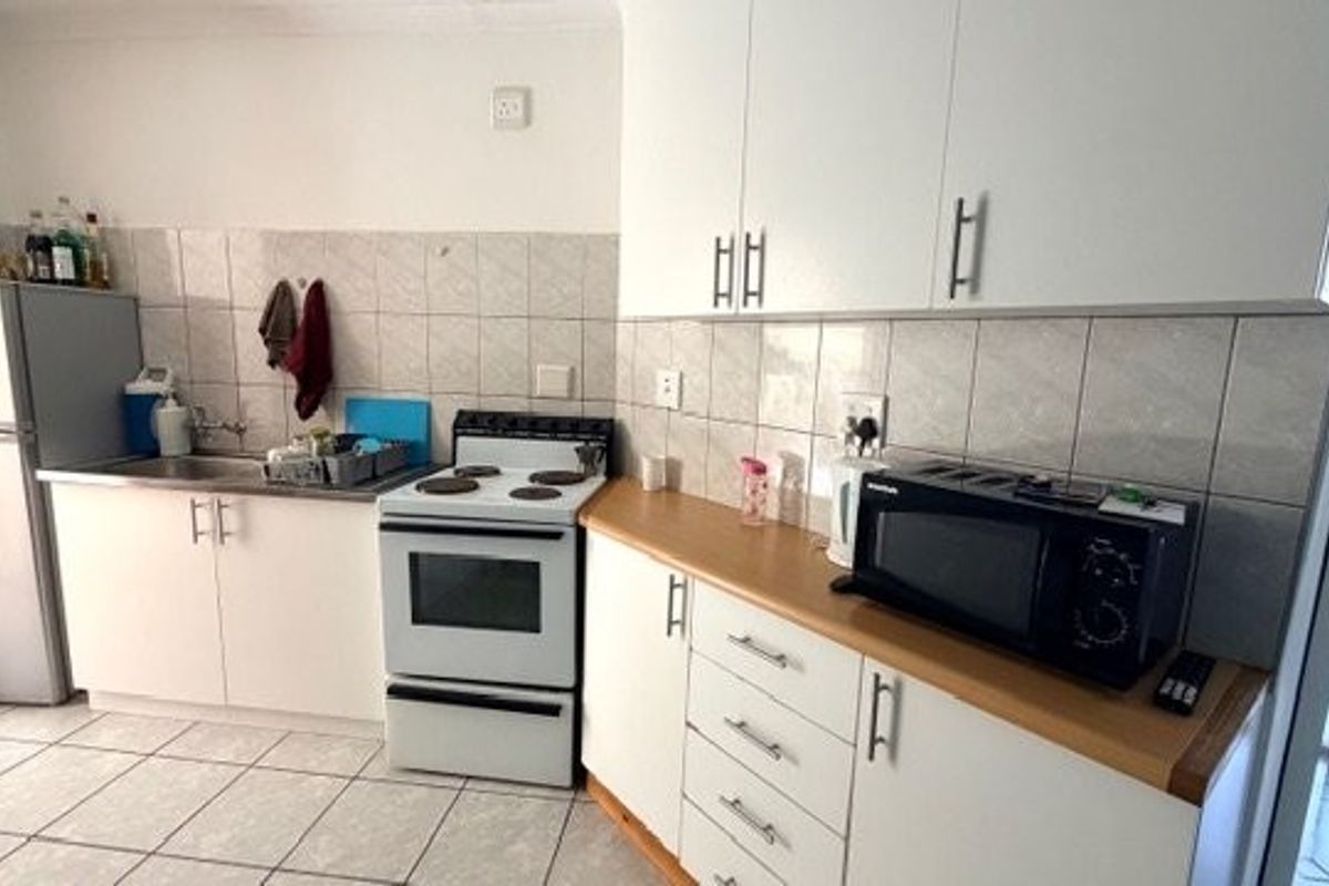 A functional kitchen featuring white cabinetry, tiled backsplash, laminate countertops, and a freestanding stove with tiled flooring.