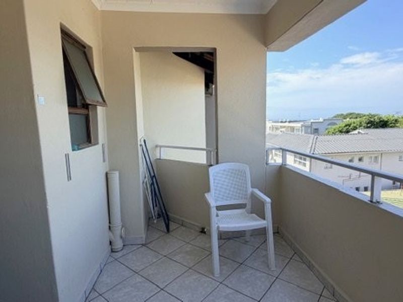 A covered balcony featuring tiled flooring and a metal balustrade, offering an outdoor space with views of the surrounding neighborhood.