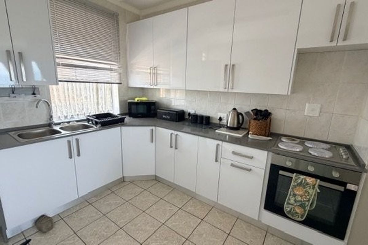 A functional kitchen featuring white high-gloss cabinetry, stone-look countertops, tiled backsplash, and a built-in oven with a four-plate electric hob.
