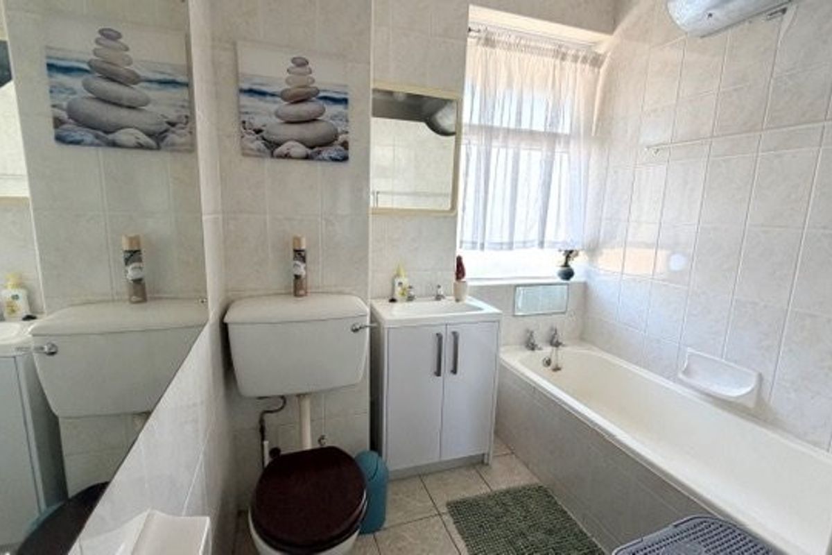 A functional bathroom featuring a standard bathtub, vanity cabinet with integrated sink, and a toilet, finished with neutral wall tiling.