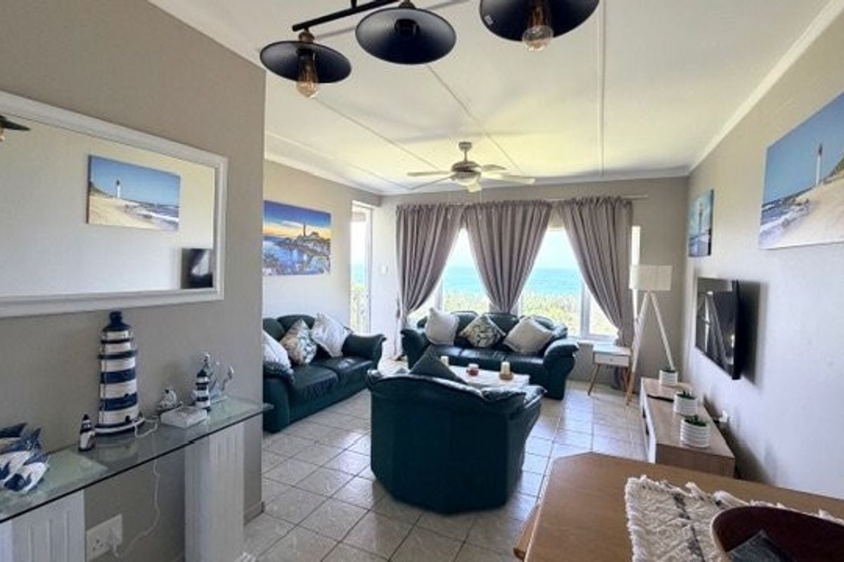 A comfortable living room featuring tiled flooring, a ceiling fan, and large windows that offer a scenic ocean view.