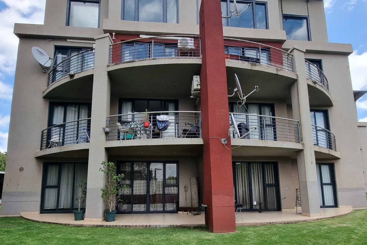 Rear elevation of a multi-story apartment building featuring stacked balconies with stainless steel railings, sliding glass doors, and a ground-level tiled patio area.