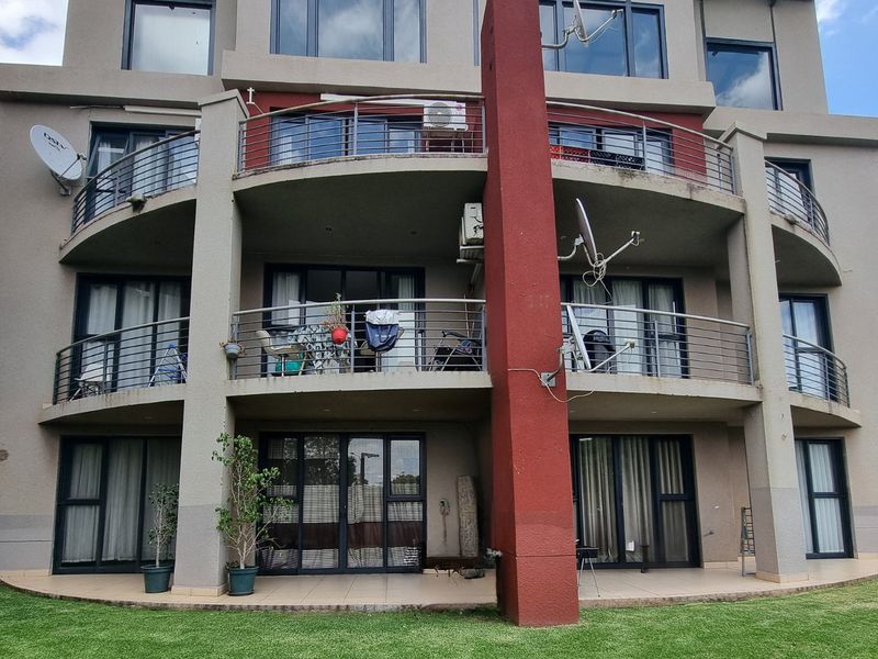 Rear elevation of a multi-story apartment building featuring stacked balconies with stainless steel railings, sliding glass doors, and a ground-level tiled patio area.