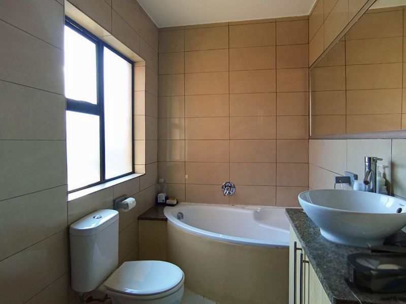 A functional bathroom featuring a built-in bathtub, vessel sink on a stone vanity, and neutral ceramic wall tiling.