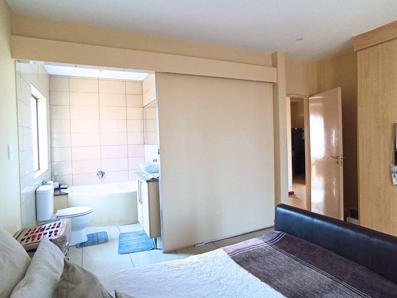 Bedroom featuring an open-plan en-suite bathroom with a bathtub, vanity, and toilet, complemented by built-in wooden wardrobes.