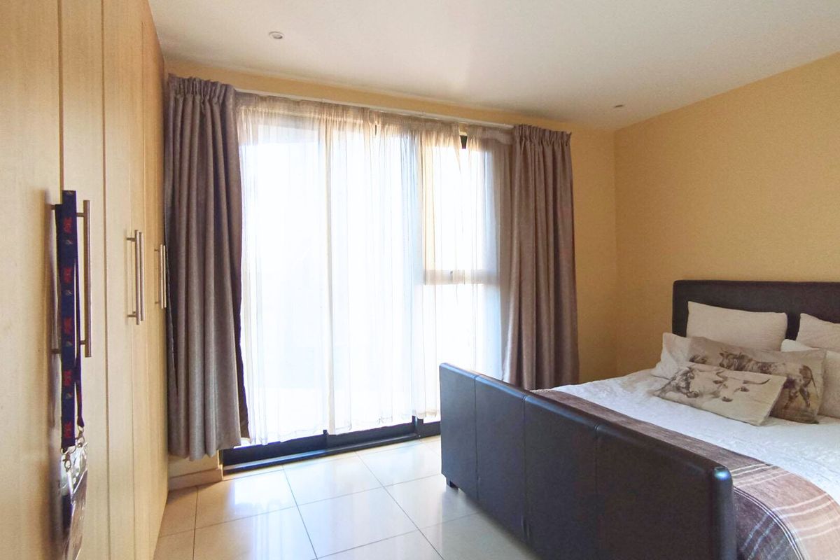 A well-lit bedroom featuring tiled flooring, built-in cupboards, and a large sliding glass door providing access to the outdoors.