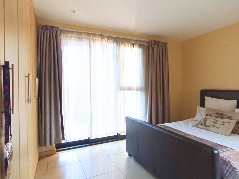 A well-lit bedroom featuring tiled flooring, built-in cupboards, and a large sliding glass door providing access to the outdoors.