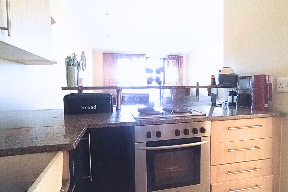A functional kitchen featuring granite countertops, built-in oven, electric hob, and light wood cabinetry, with an open-plan layout overlooking the living area.