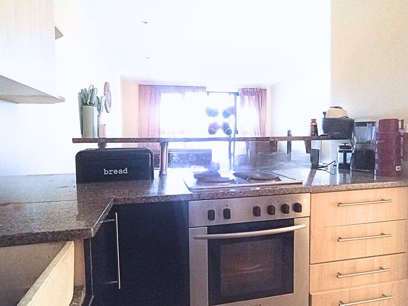 A functional kitchen featuring granite countertops, built-in oven, electric hob, and light wood cabinetry, with an open-plan layout overlooking the living area.