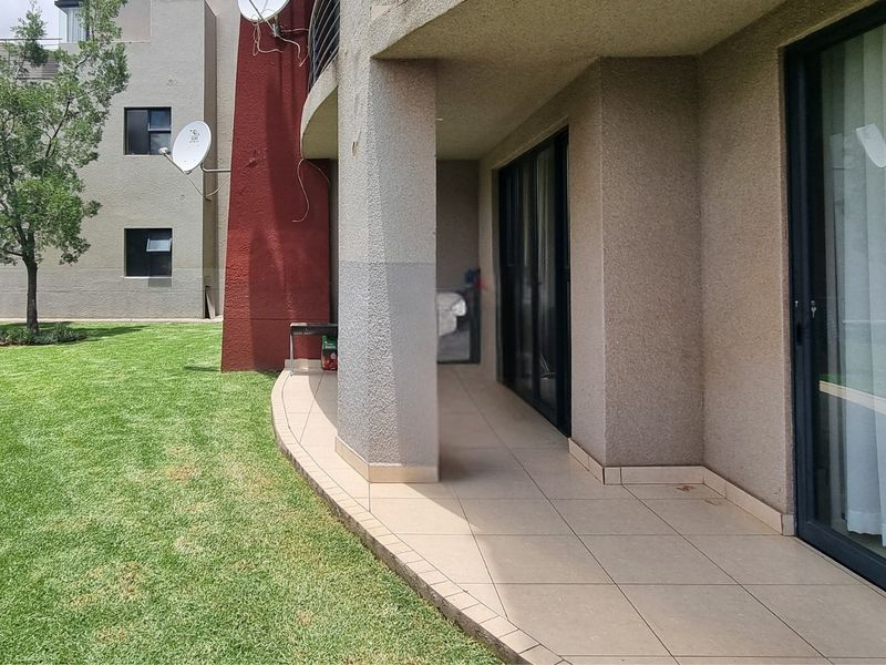 A covered ground-floor patio with tiled flooring and sliding glass door access, overlooking a communal garden area.