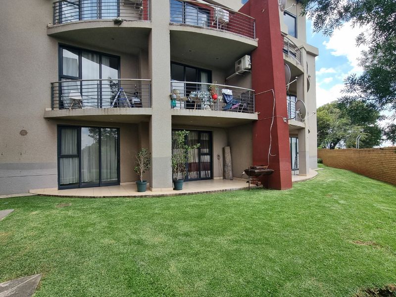 Rear view of the apartment building featuring multiple levels of balconies with stainless steel railings, sliding glass doors, and a well-maintained lawn area.