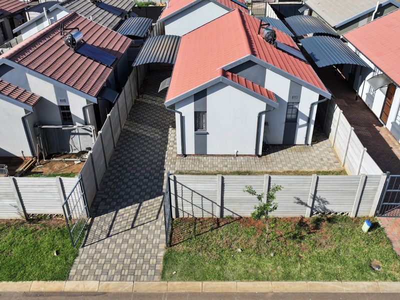 Aerial view of a residential complex featuring modern houses with tiled roofs, solar water heaters, paved driveways, and secure precast boundary walls.
