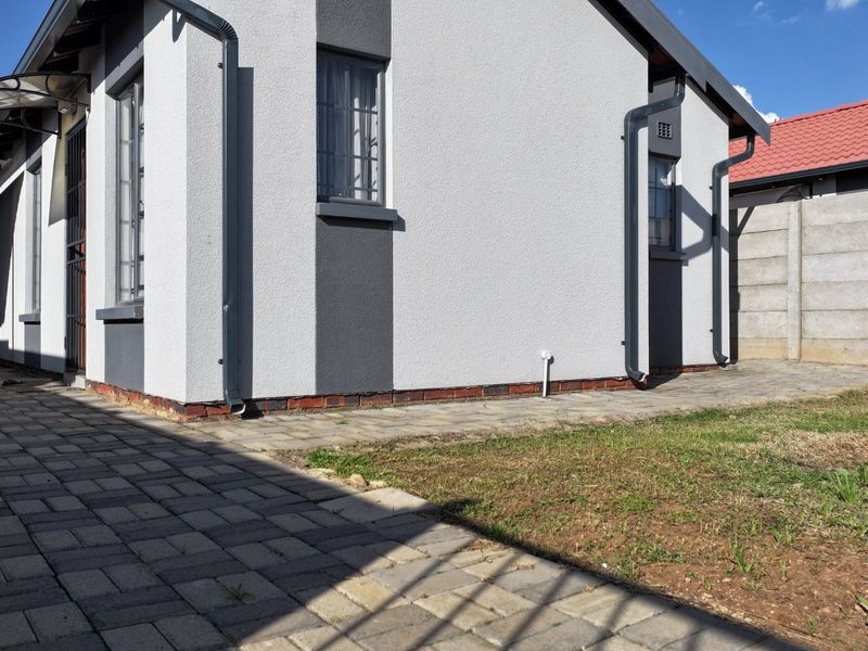 Rear exterior view of the house featuring paved areas, a small lawn, security bars on windows, and a precast concrete boundary wall.