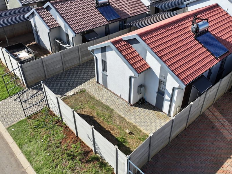 Aerial view of a residential property featuring a tiled roof with solar water heater, paved driveway, and a private enclosed garden area.