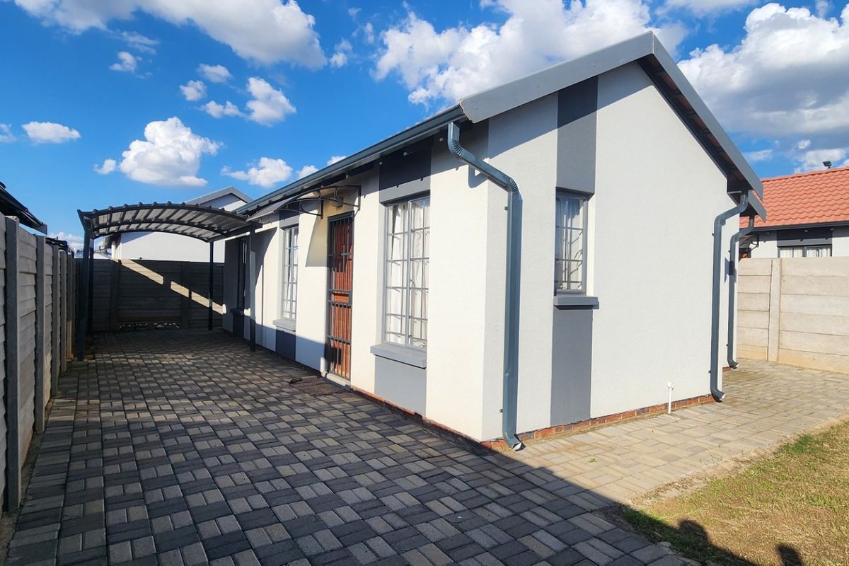 Rear exterior view of the house featuring a paved driveway, carport, and secure boundary walling.