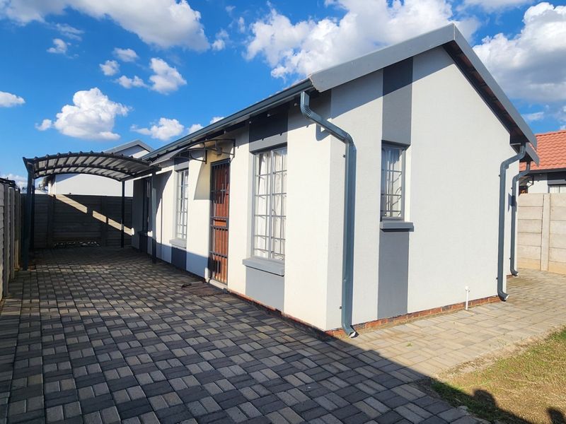 Rear exterior view of the house featuring a paved driveway, carport, and secure boundary walling.