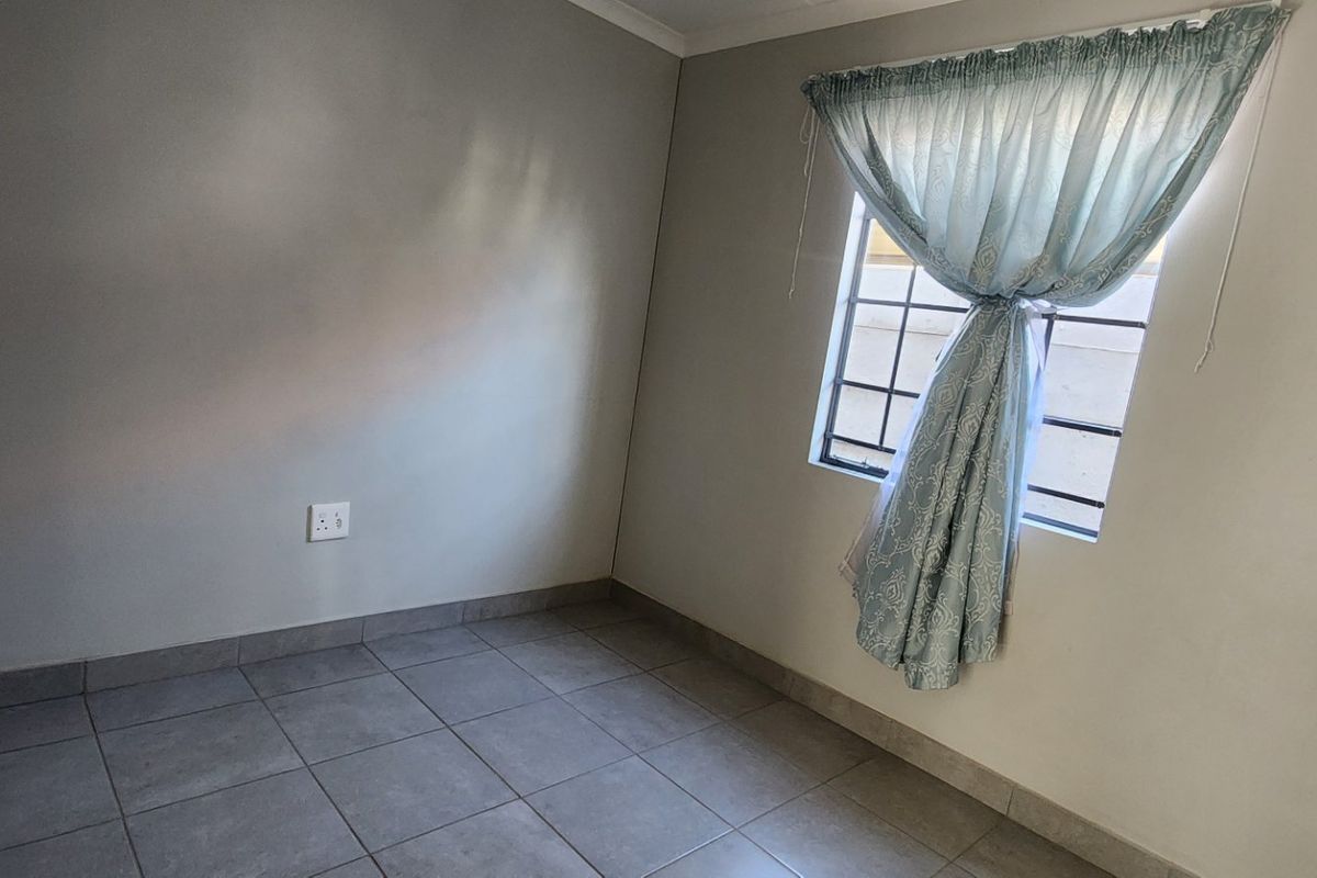 A simple, empty bedroom featuring tiled flooring and a window fitted with security bars.