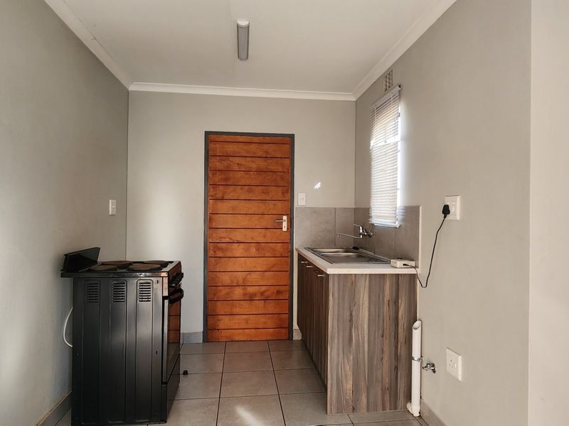 A compact kitchen area featuring tiled flooring, a freestanding stove, built-in cabinetry with a stainless steel sink, and a wooden door.