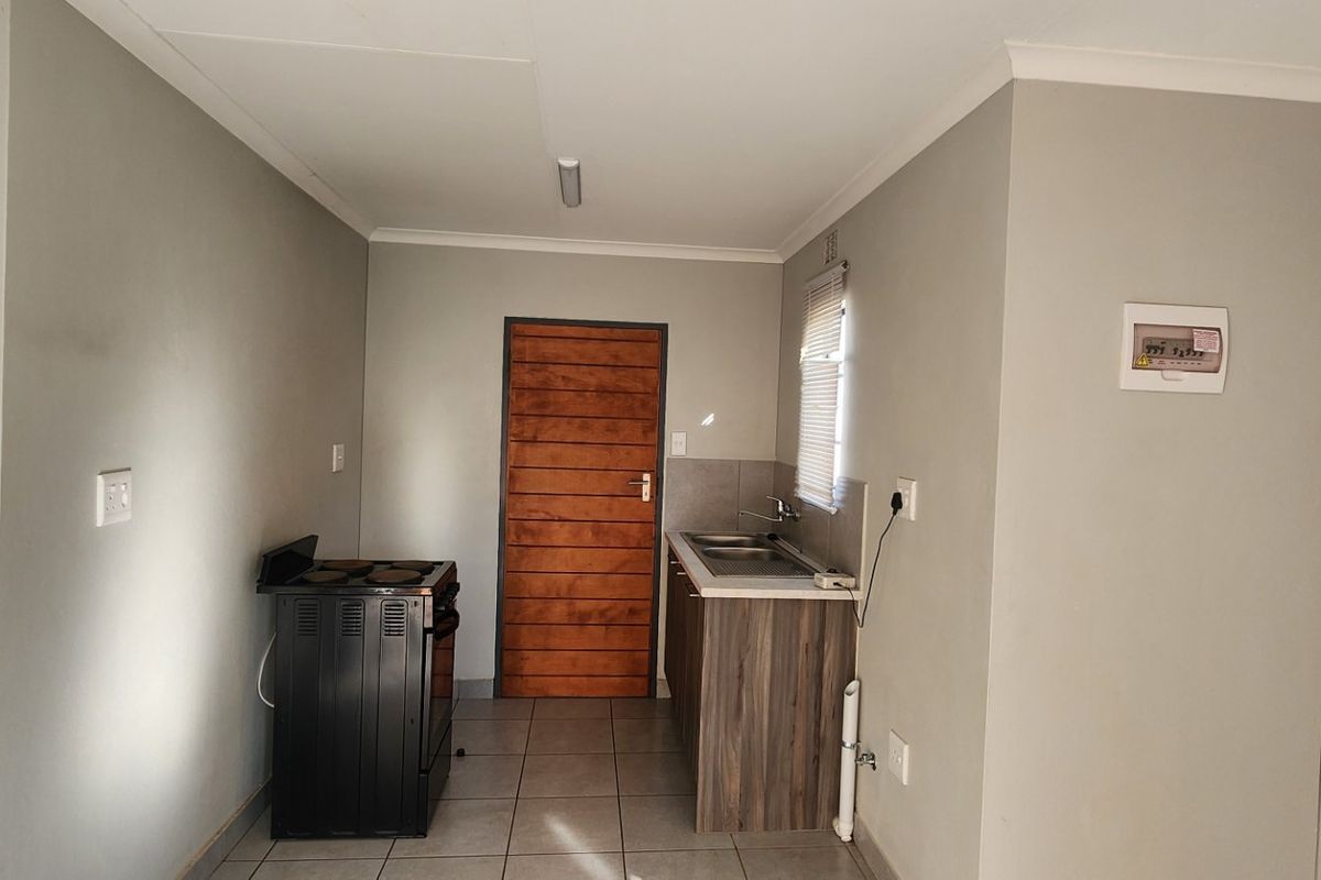 A compact kitchen area featuring tiled flooring, a small kitchenette with a sink, and a freestanding stove.