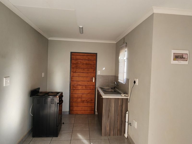 A compact kitchen area featuring tiled flooring, a small kitchenette with a sink, and a freestanding stove.