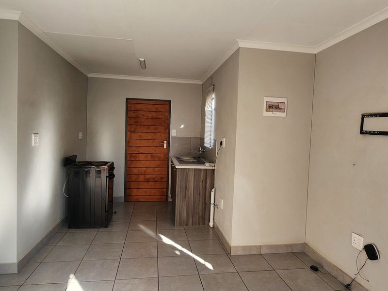 An open-plan living and kitchen area featuring tiled flooring, a compact kitchenette with a sink, and a freestanding stove.