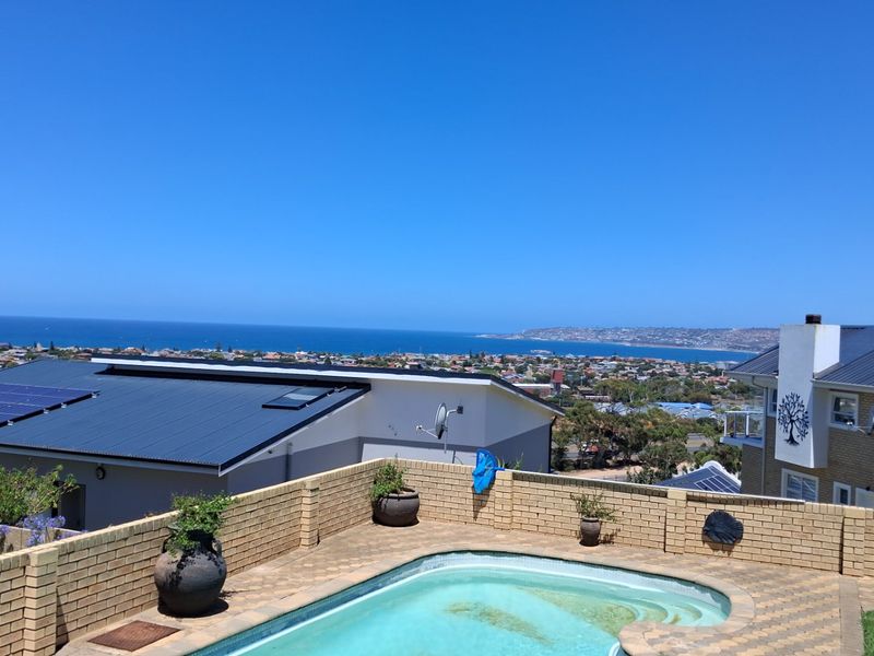Outdoor pool area featuring a brick boundary wall and expansive coastal views, set against a backdrop of residential rooftops.